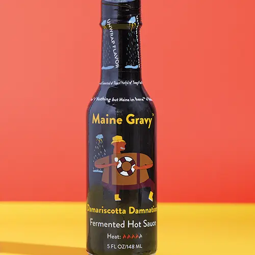 Maine Gravy Damariscotta Damnation hot sauce bottle on a colored background