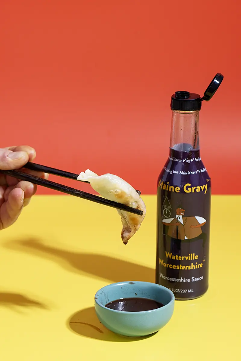 Dumpling held by chopsticks over small bowl after dip in Maine Gravy Waterville Worcester sauce
